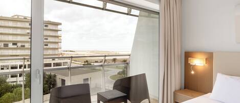 A hotel room with a balcony, a bed, a nightstand, and a view of the cityscape.
