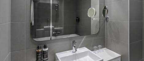 A modern bathroom with a white sink, a mirror, and a shower enclosure.