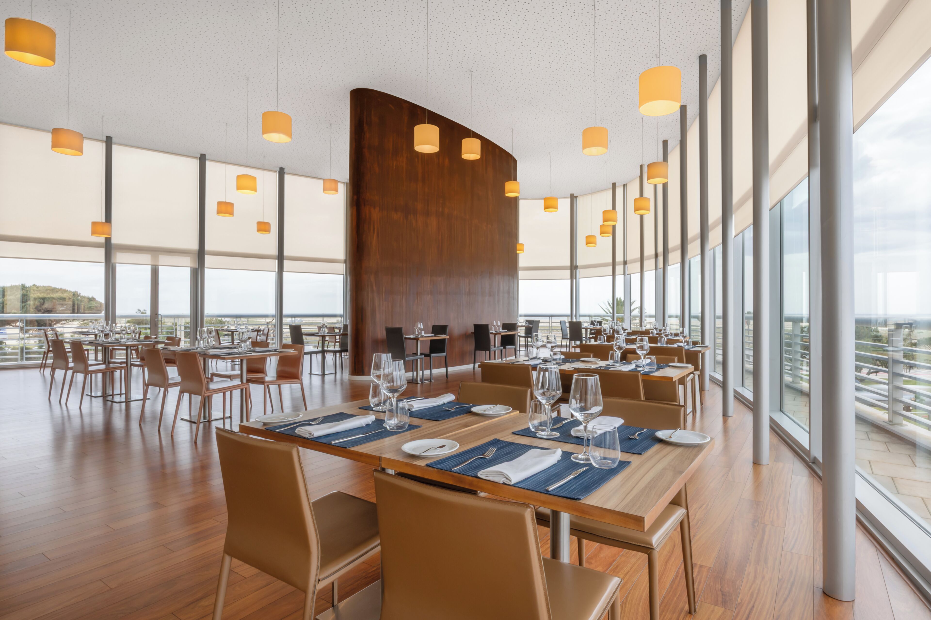 A spacious dining area with long tables, chairs, and pendant lighting.