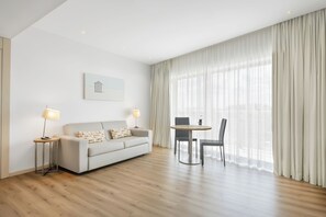A modern hotel room with a sofa, a small table, a chair, and a large window with curtains. - Eurostars Oasis Plaza Hotel (Figueira da Foz)
