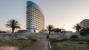 A modern hotel with a curved facade, multiple balconies, and a wooden boardwalk leading to the entrance.