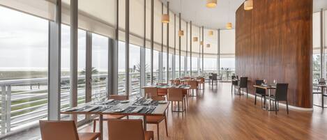 A modern restaurant with high ceilings, large windows, and a view of the cityscape.