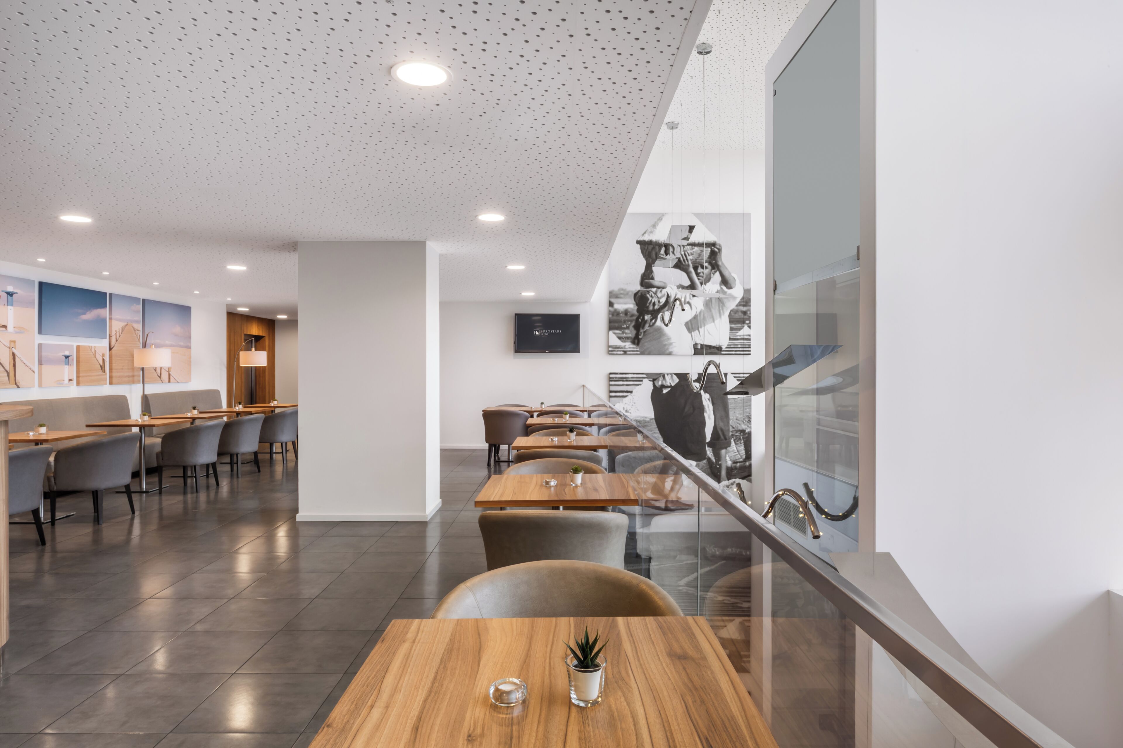 Ein modernes Restaurant mit hoher Decke, eingelassener Beleuchtung und einer Mischung aus Holz- und Polstermöbeln.