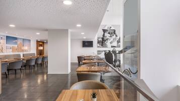 A modern restaurant with a high ceiling, recessed lighting, and a mix of wooden and upholstered seating.