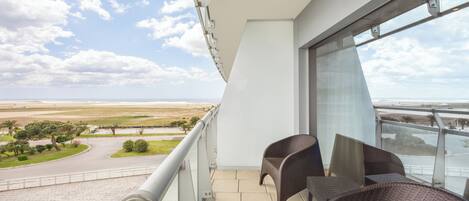 Un balcon avec des fauteuils en osier, une vue sur la plage et un ciel dégagé.