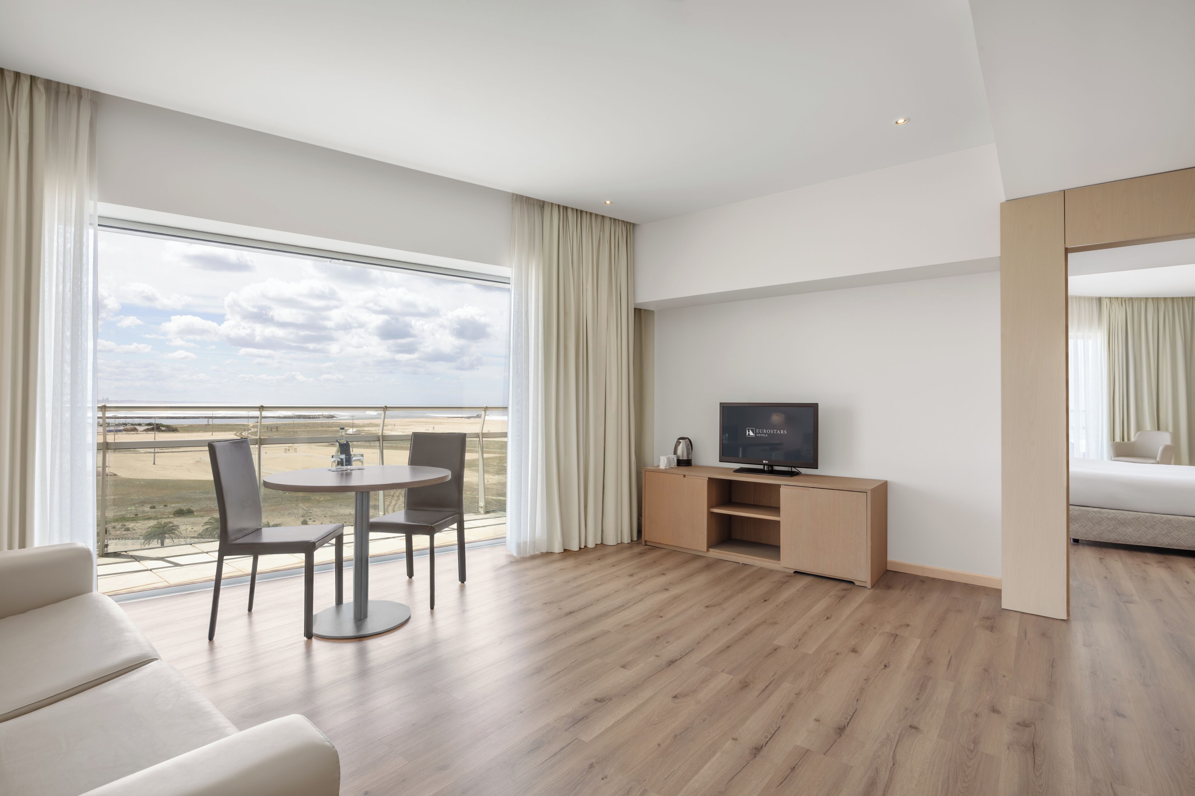 A hotel room with a balcony, a TV, a desk, and a sofa.