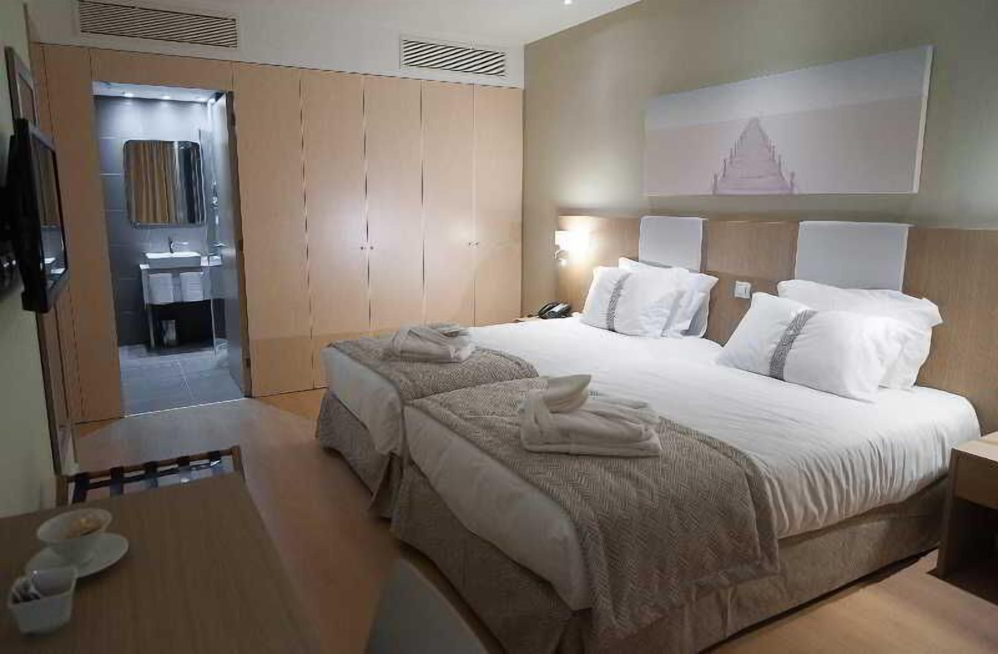 A hotel room with a large bed, a bedside table, a nightstand, a mirror, and a wardrobe.