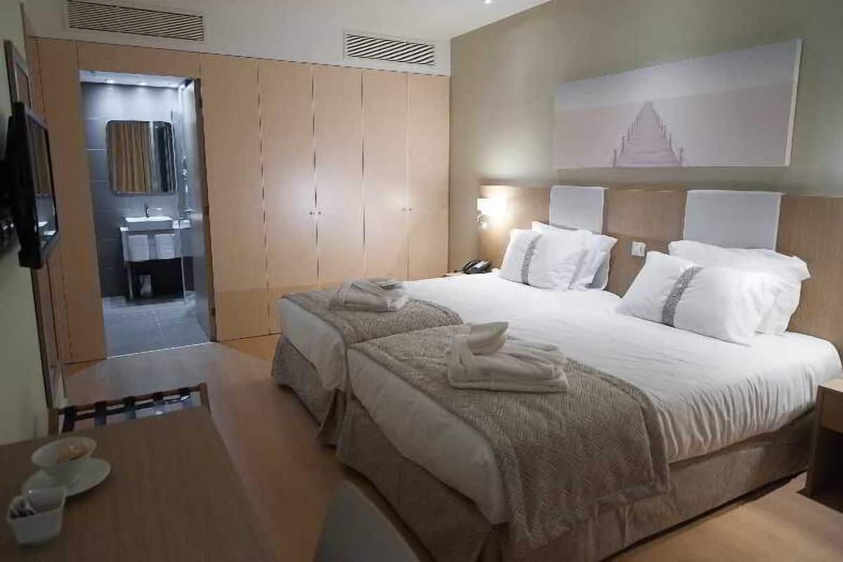 A hotel room with a large bed, a bedside table, a nightstand, a mirror, and a wardrobe.