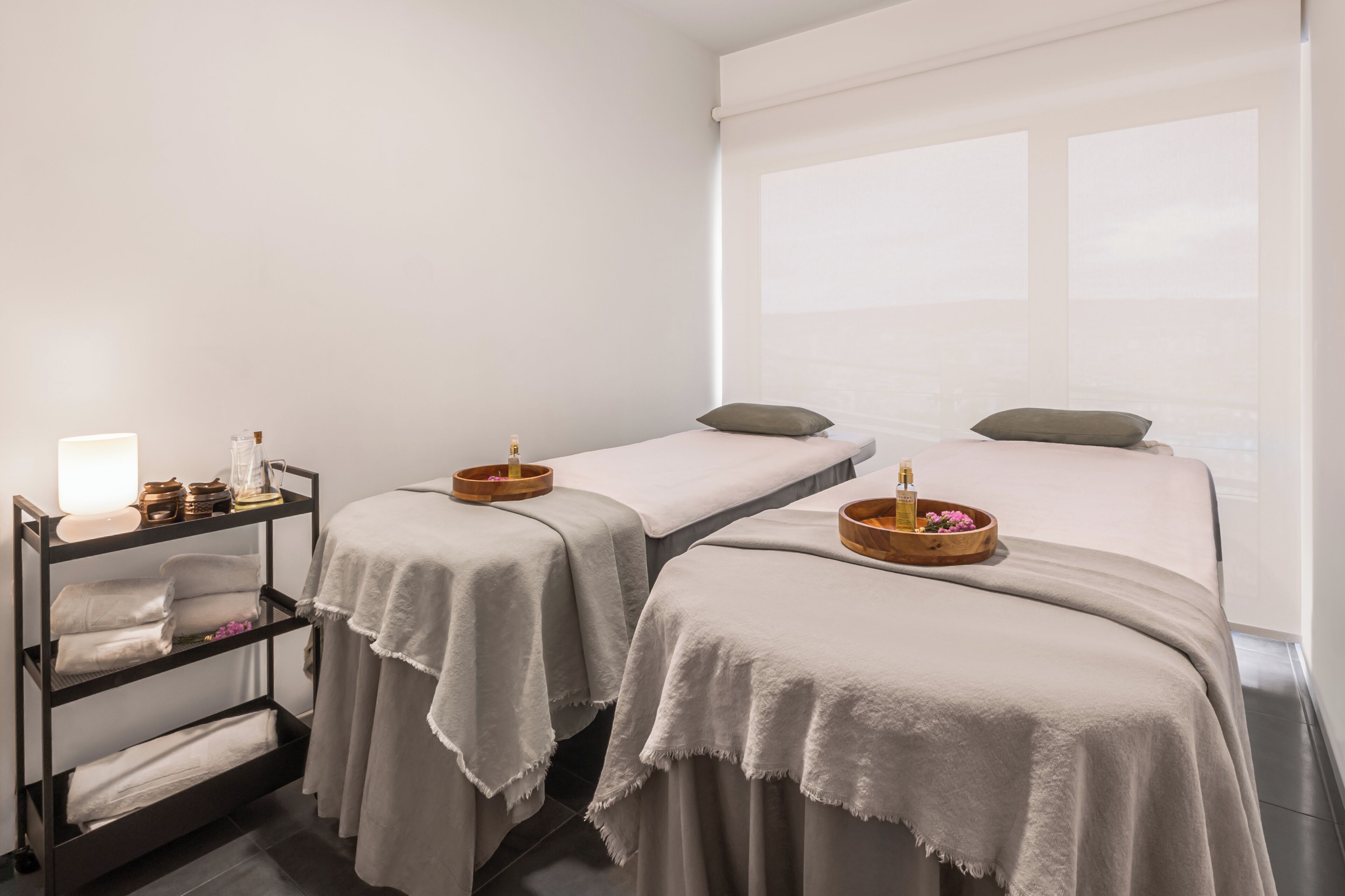 A spa room with two beds, a shelf with towels, and a window with a view.