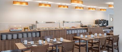 Un espace moderne dédié au petit-déjeuner, avec des tables et des chaises en bois, un buffet et un éclairage suspendu.