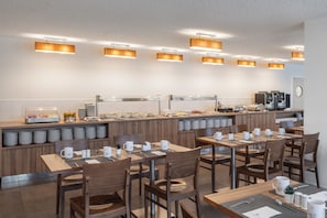 A modern breakfast area with wooden tables and chairs, a buffet counter, and overhead lighting. - Eurostars Oasis Plaza Hotel (Figueira da Foz)