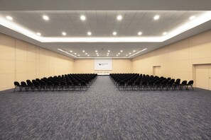 A conference room with rows of chairs, a projector screen, and a presentation area. - Eurostars Oasis Plaza Hotel (Figueira da Foz)