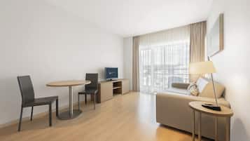 Quarto de hotel moderno com sofá, uma mesinha redonda, televisão e luminária.