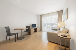 A modern hotel room with a sofa, a small round table, a TV, and a lamp. - Eurostars Oasis Plaza Hotel (Figueira da Foz)