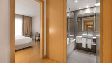 Una habitación de hotel moderna con cama, escritorio y baño con espejo, lavamanos y toallero.