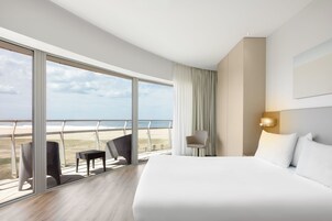 Habitación de hotel con una cama grande, un área de descanso con sillas y vista a la playa.