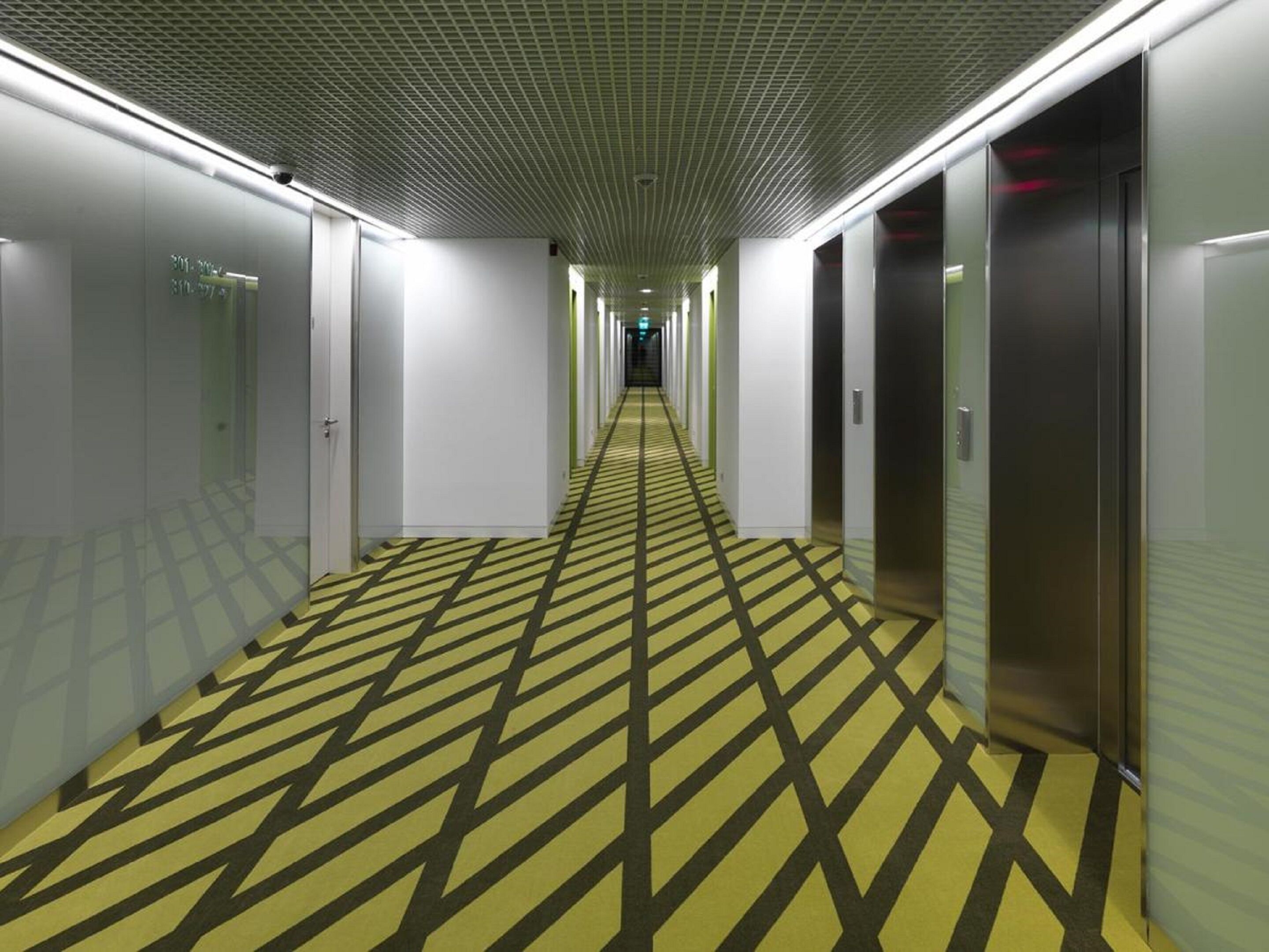 A hotel corridor with a patterned carpet, doors, and elevators.