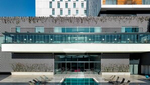 Un hotel moderno con piscina en la azotea, fachada de cristal y una combinación de elementos blancos y de madera en el exterior.