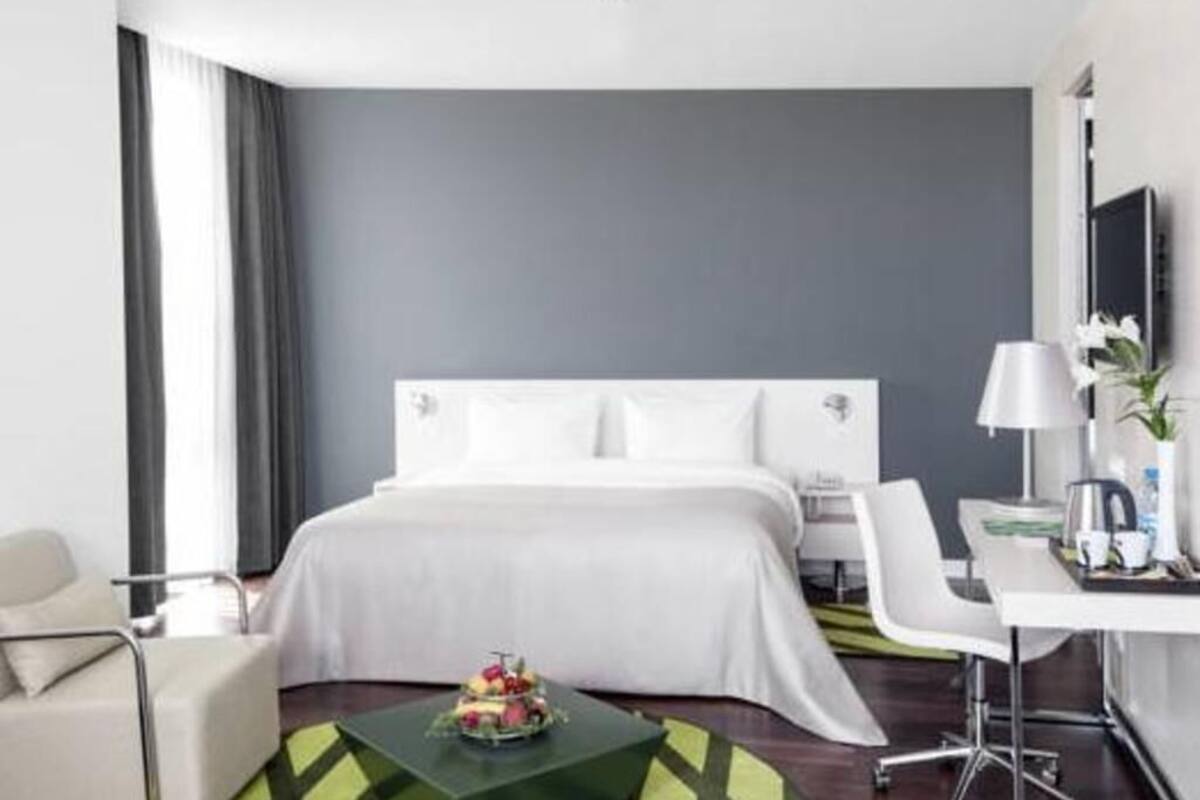 A modern hotel room with a large bed, a desk, a chair, and a small table with a fruit arrangement.