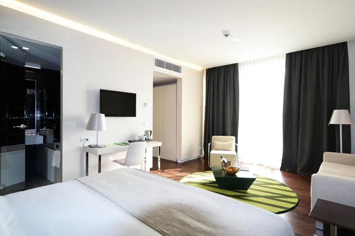 Habitación de hotel con cama, escritorio, silla, televisor y vista de la ciudad por la noche.