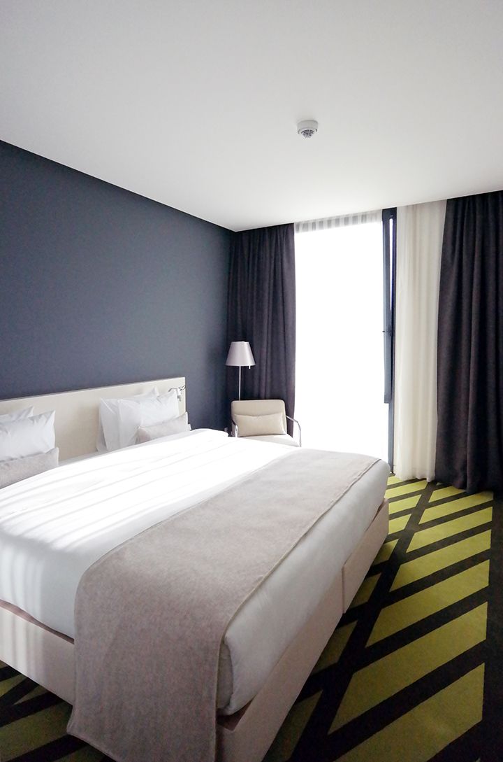 A hotel room with a large bed, a chair, a lamp, and a window with curtains.