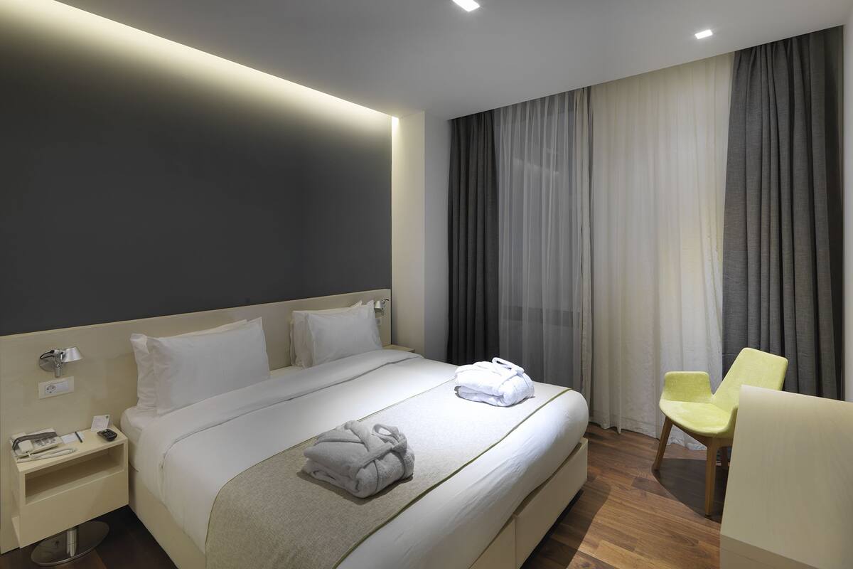 A modern hotel room with a large bed, a bedside table with a lamp, and a chair.