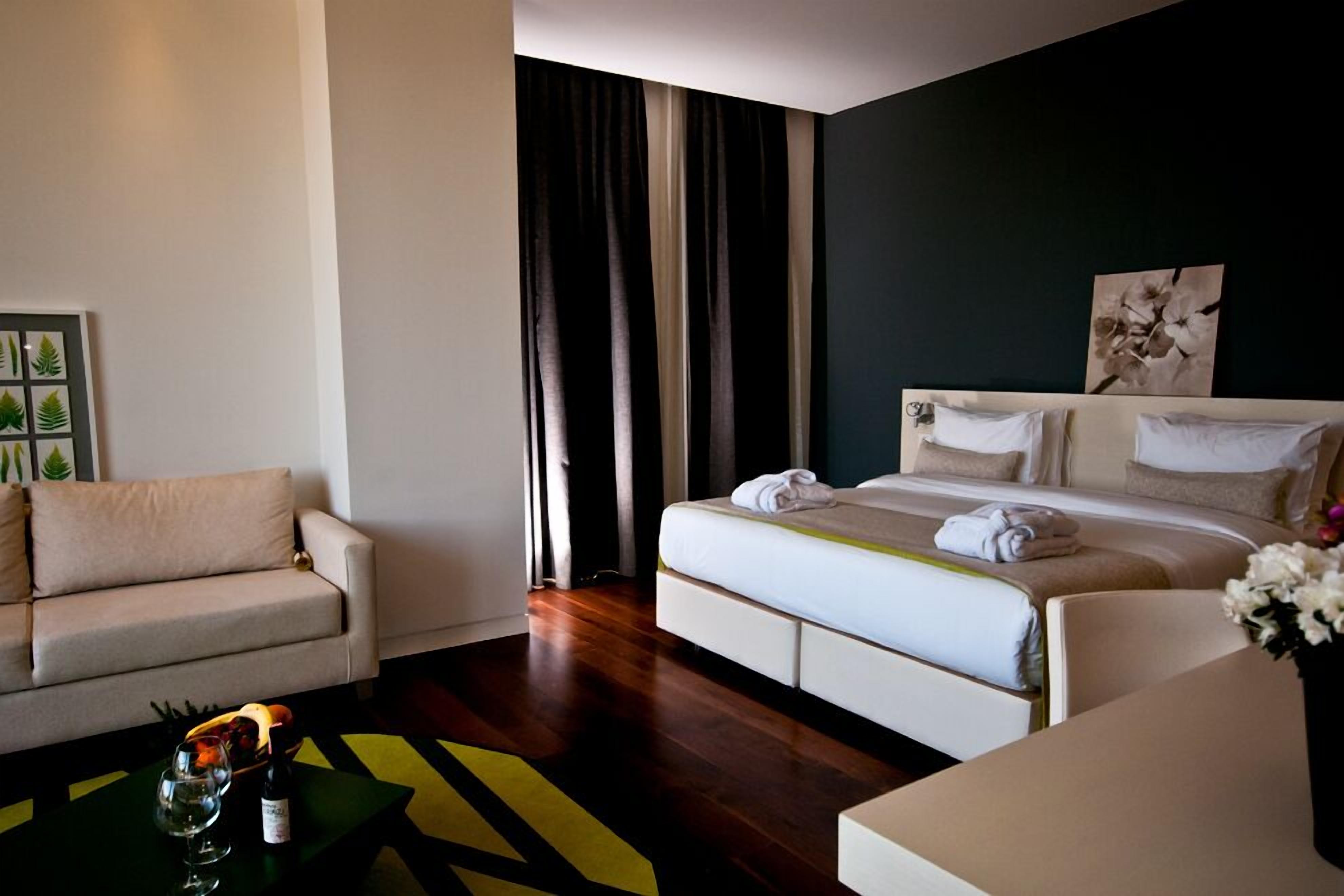 Una habitación de hotel moderna con una cama, un sofá y una mesa de centro con una botella y un vaso.