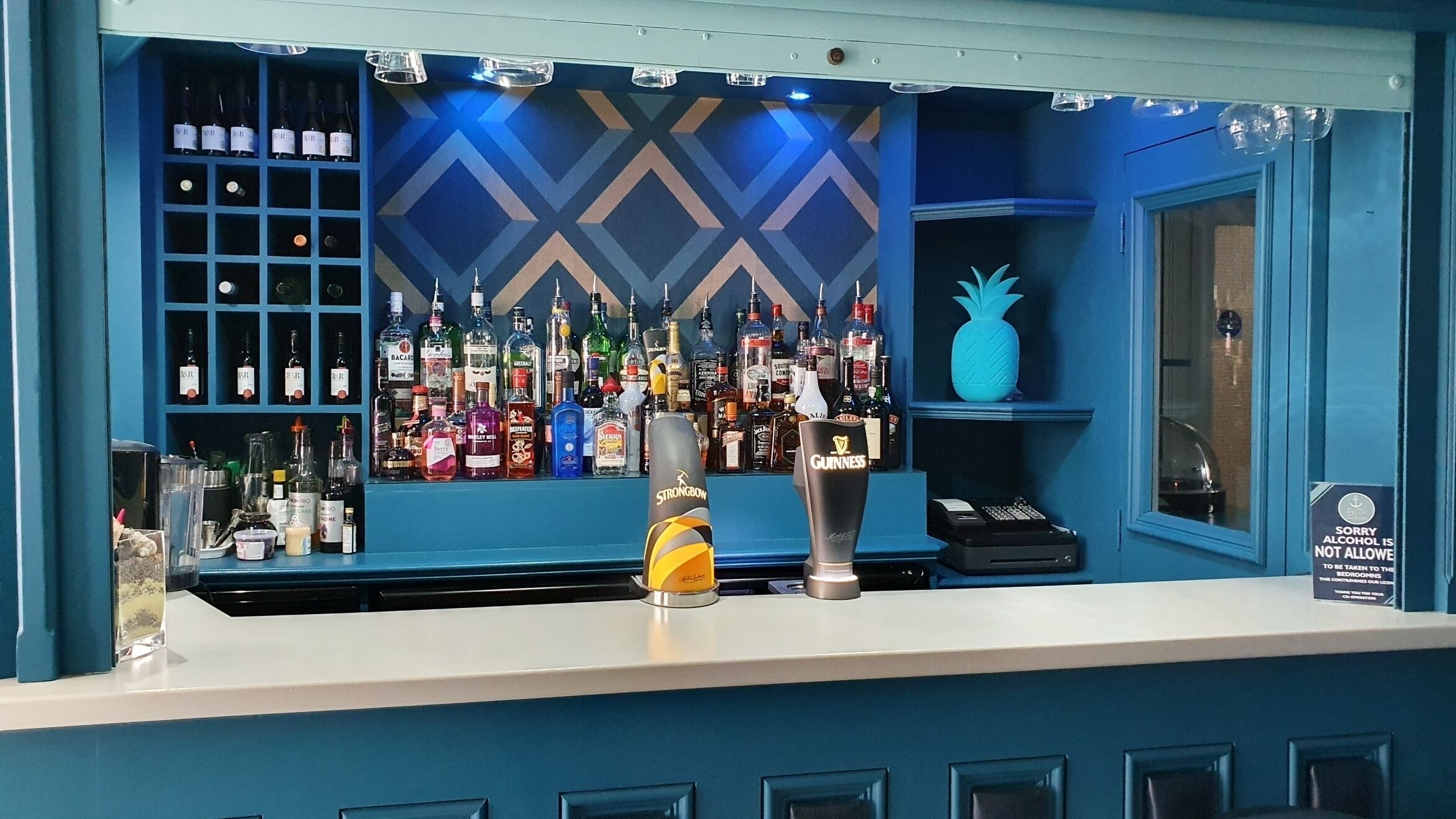 A bar area with a blue color scheme, various liquor bottles, and a pineapple decoration.