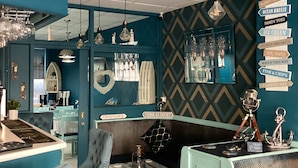 Interior de restaurante con temática náutica, paredes color turquesa, muebles antiguos y decoración marítima.
