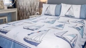 Un dormitorio con una cama que presenta un edredón con motivos náuticos, una pared de textura de madera y un techo con iluminación empotrada.