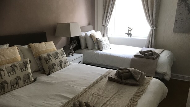 Een hotelkamer met twee bedden, een nachtkastje, een lamp en een raam met gordijnen.