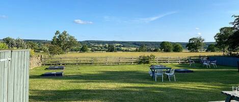A grassy outdoor area with a wooden fence, a picnic table, and chairs.