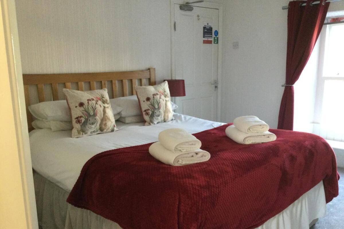 A neatly made bed with a red blanket, two pillows with floral designs, and two folded towels.