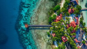 An aerial view of a coastal resort with a long pier extending into turquoise waters, surrounded by lush greenery and red-roofed buildings. - Ray Caye Private Island Resort (Placencia)