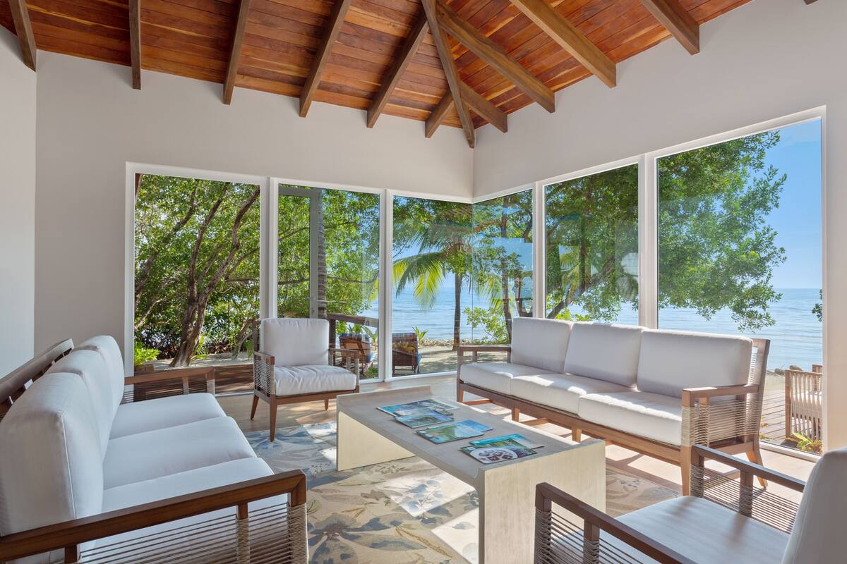 A spacious living area with a wooden ceiling, large windows, a white sofa, and a coffee table with magazines.