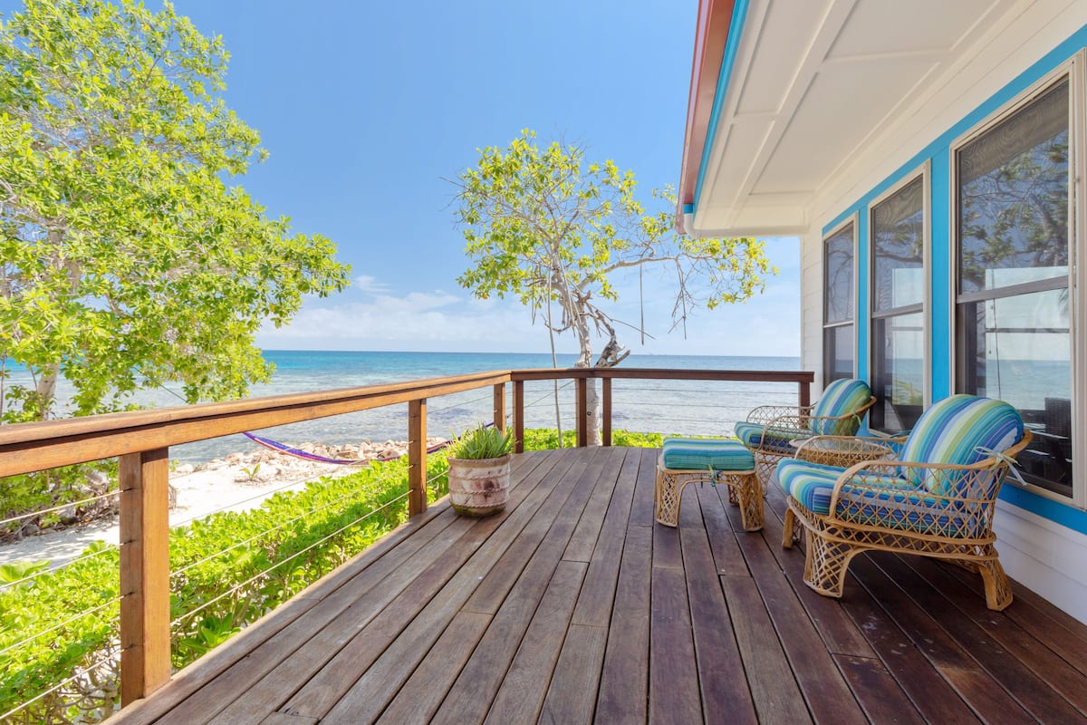 A wooden deck with wicker furniture overlooking a beach.