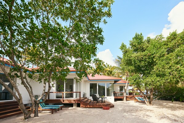 A beachfront property with a covered deck, lounge chairs, and a small table. - Ray Caye Private Island Resort (Placencia)