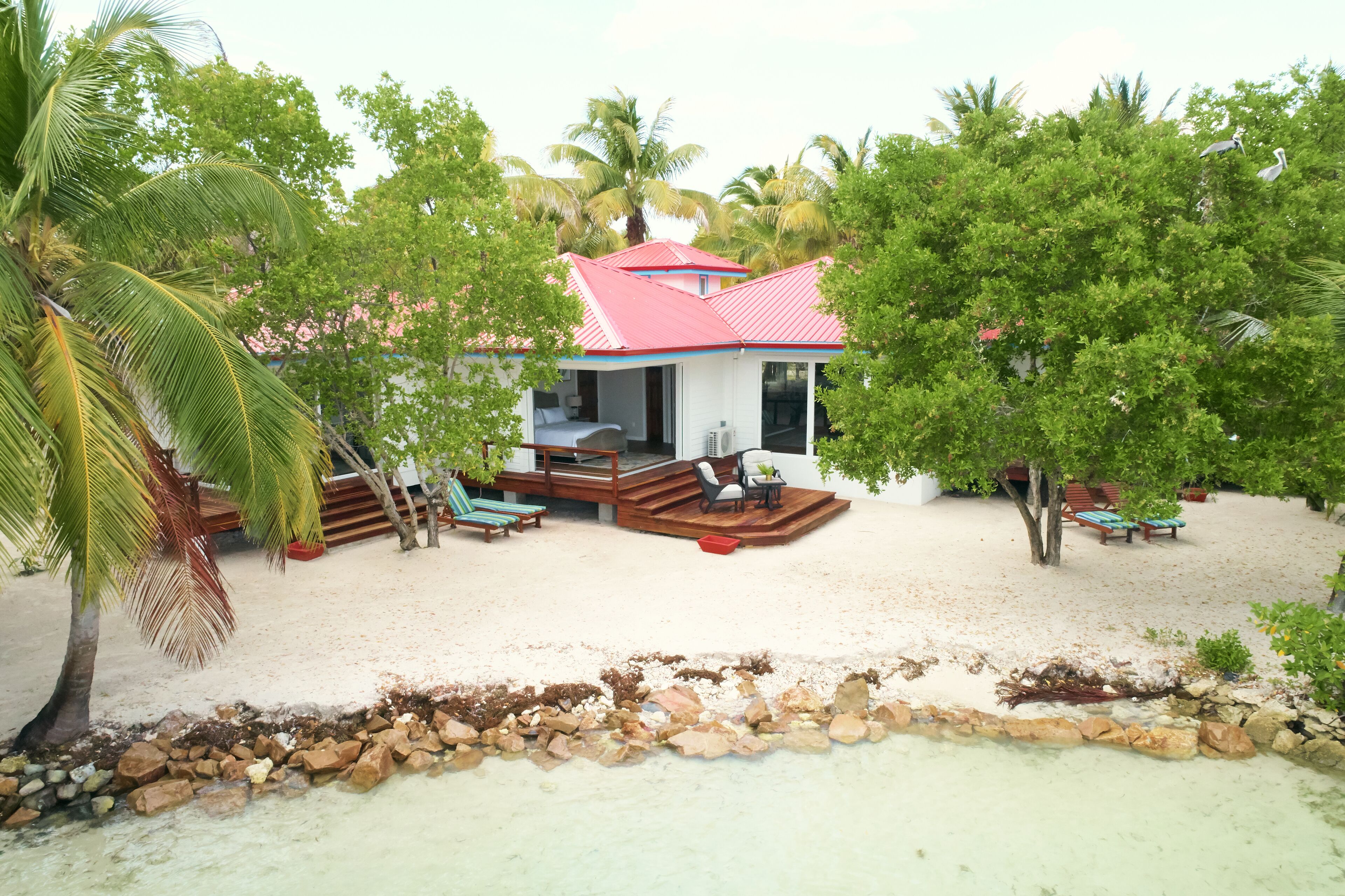 A beachfront property with a red-roofed building, a sandy beach, and palm trees.