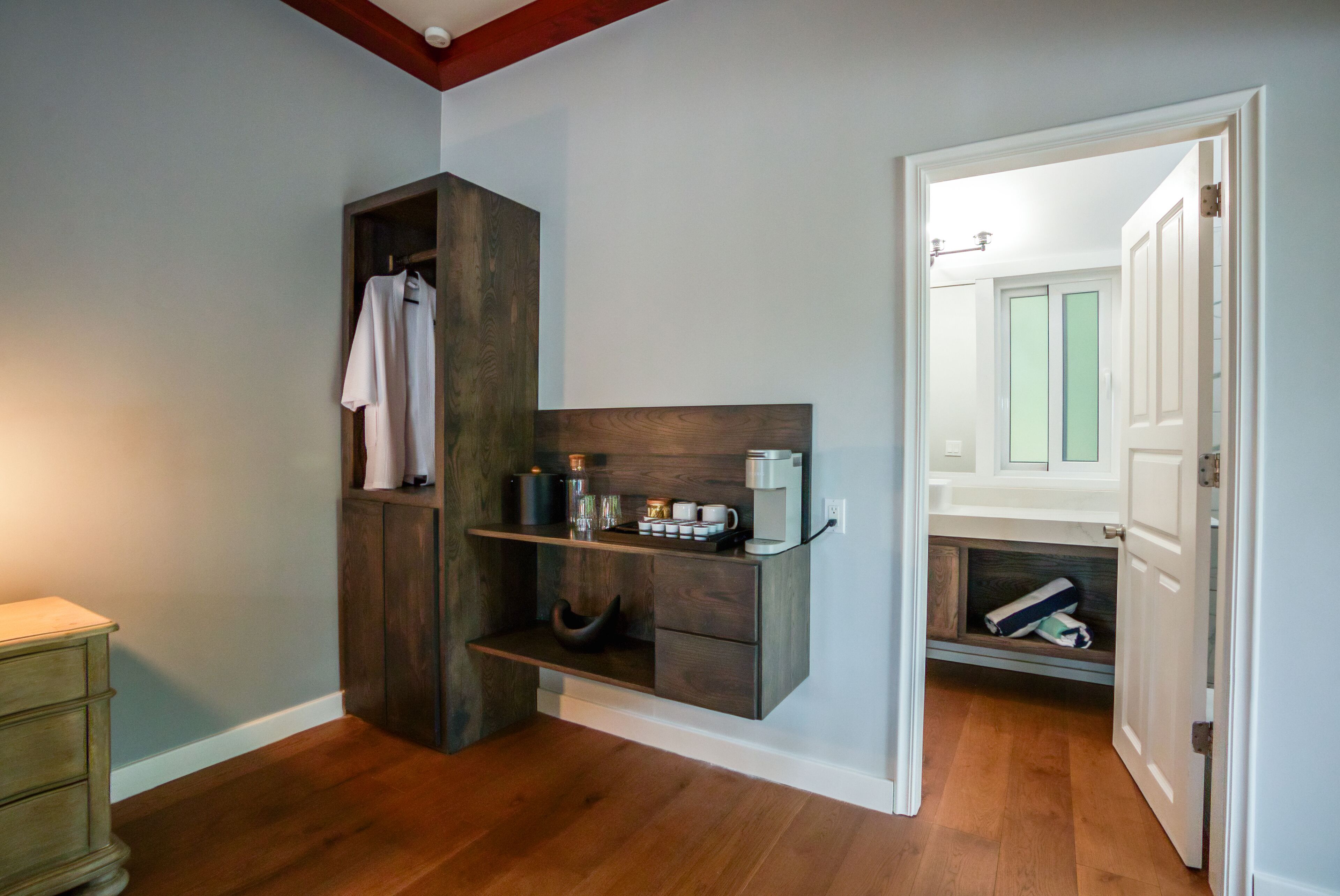 Un baño pequeño con tocador de madera, perchero y zona de ducha visible a través de una puerta abierta.