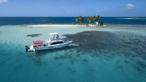 Un bote en aguas turquesas cristalinas, con una playa arenosa y palmeras al fondo.