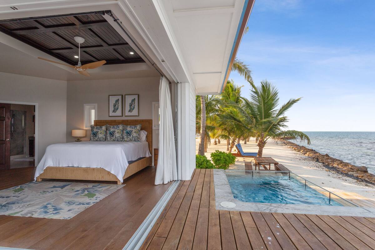 A bedroom with a large bed, a ceiling fan, and a view of the ocean.