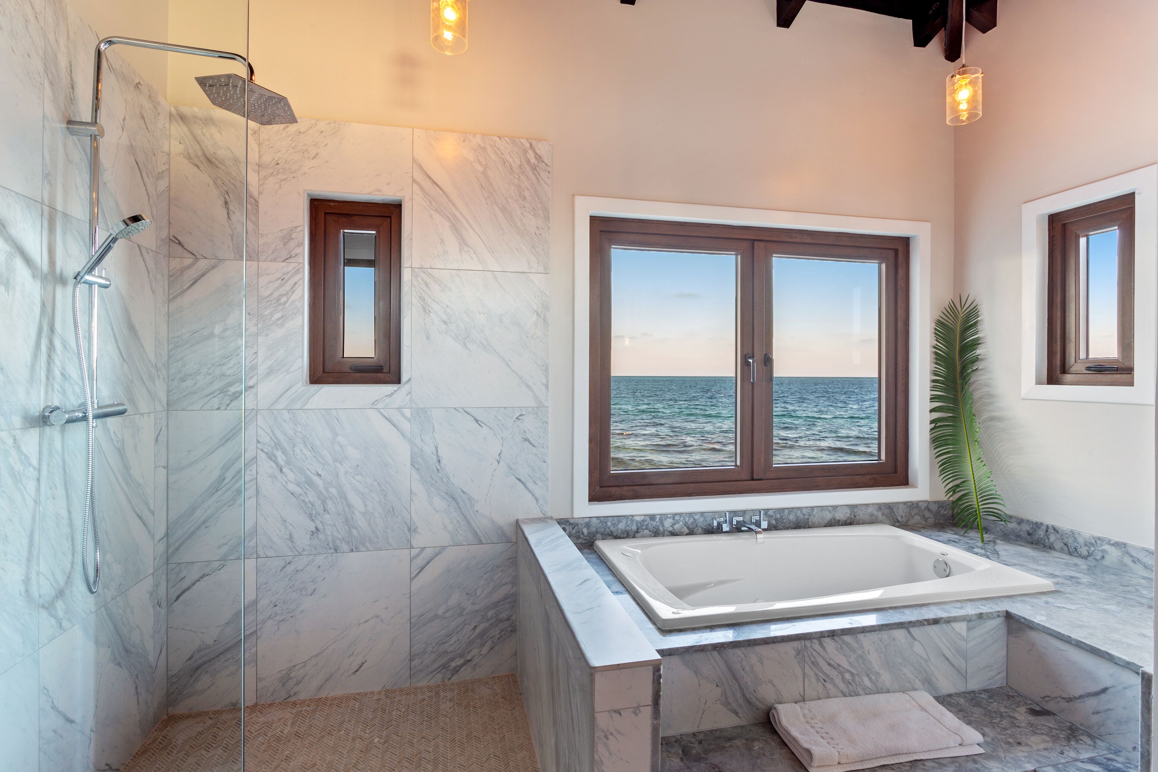Un baño con una bañera grande, ducha y vista al mar por una ventana.
