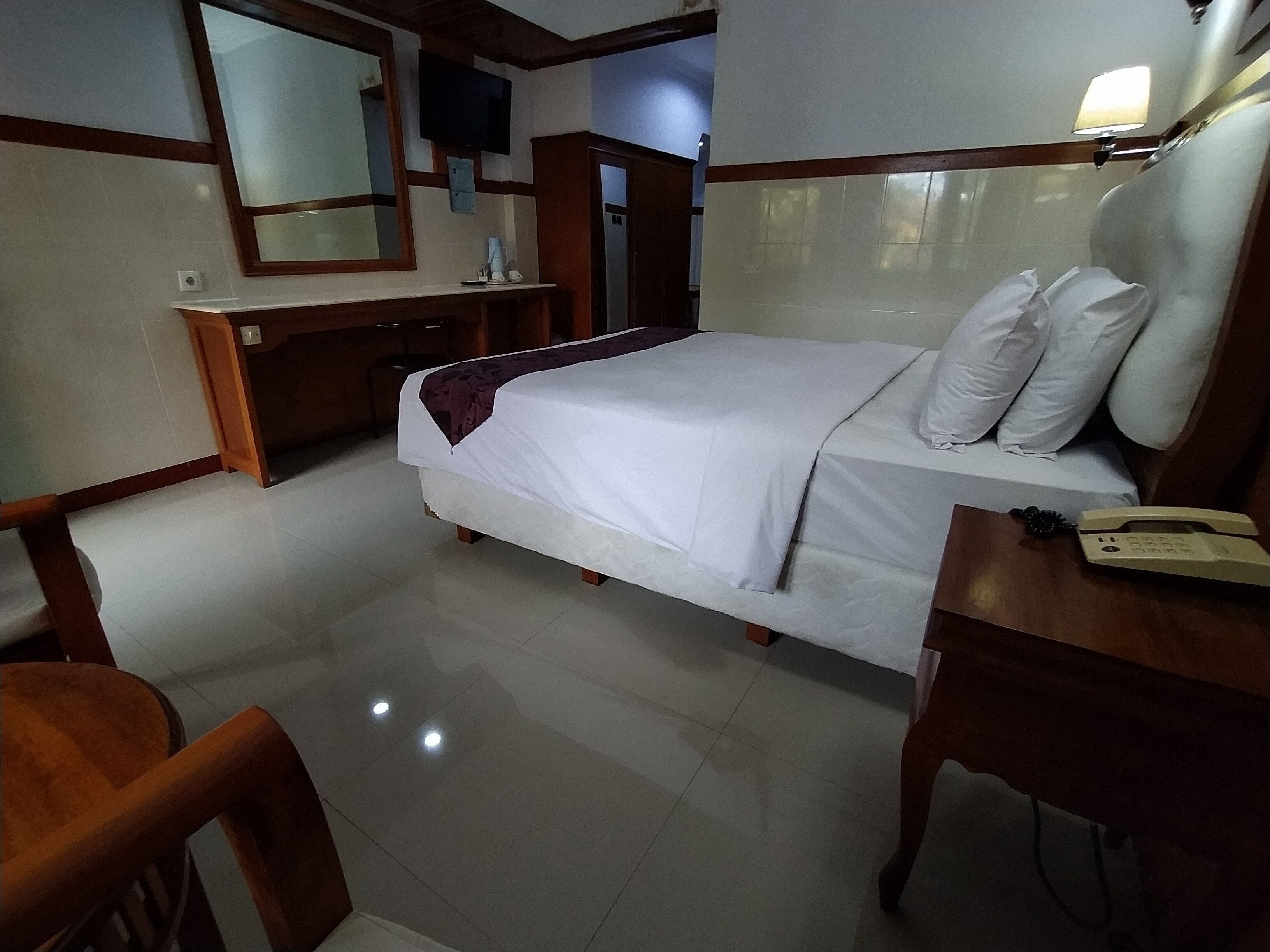 Une chambre d’hôtel équipée d’un lit, d’une table de chevet, d’une chaise, d’un bureau et d’un téléviseur fixé au mur.