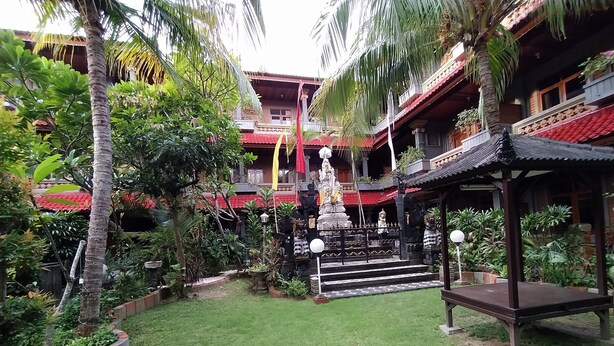 A courtyard with a statue, a gazebo, and a building with a red roof. - Hotel Sorga (Kuta)