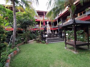 Un patio con una estatua, un pabellón y un edificio de techo rojo.
