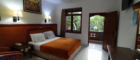 A hotel room with a bed, bedside lamps, a desk, and a view of greenery outside.