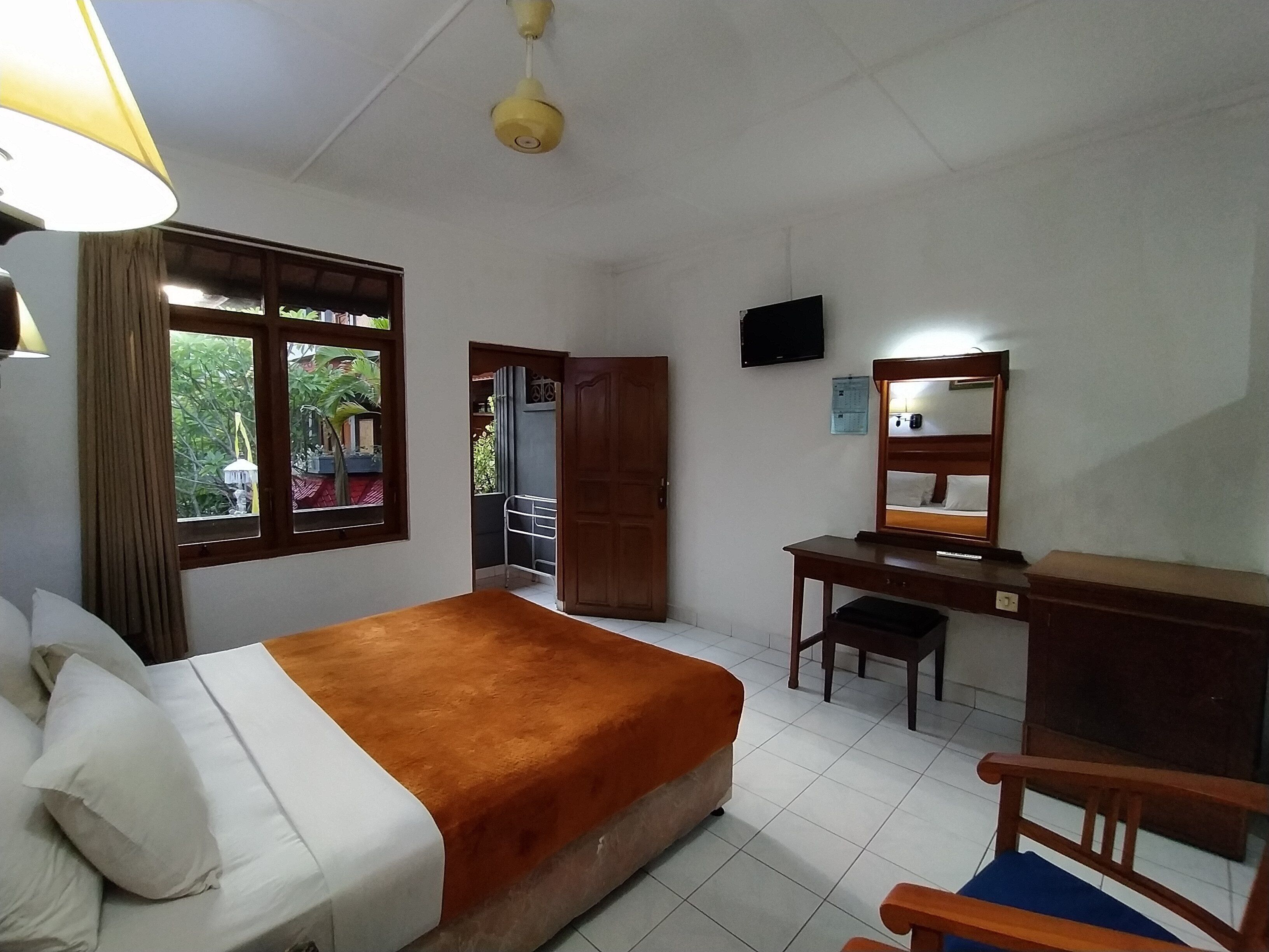 A hotel room with a bed, desk, chair, TV, and a window with a view of greenery.