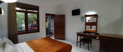 A hotel room with a bed, desk, chair, TV, and a window with a view of greenery.