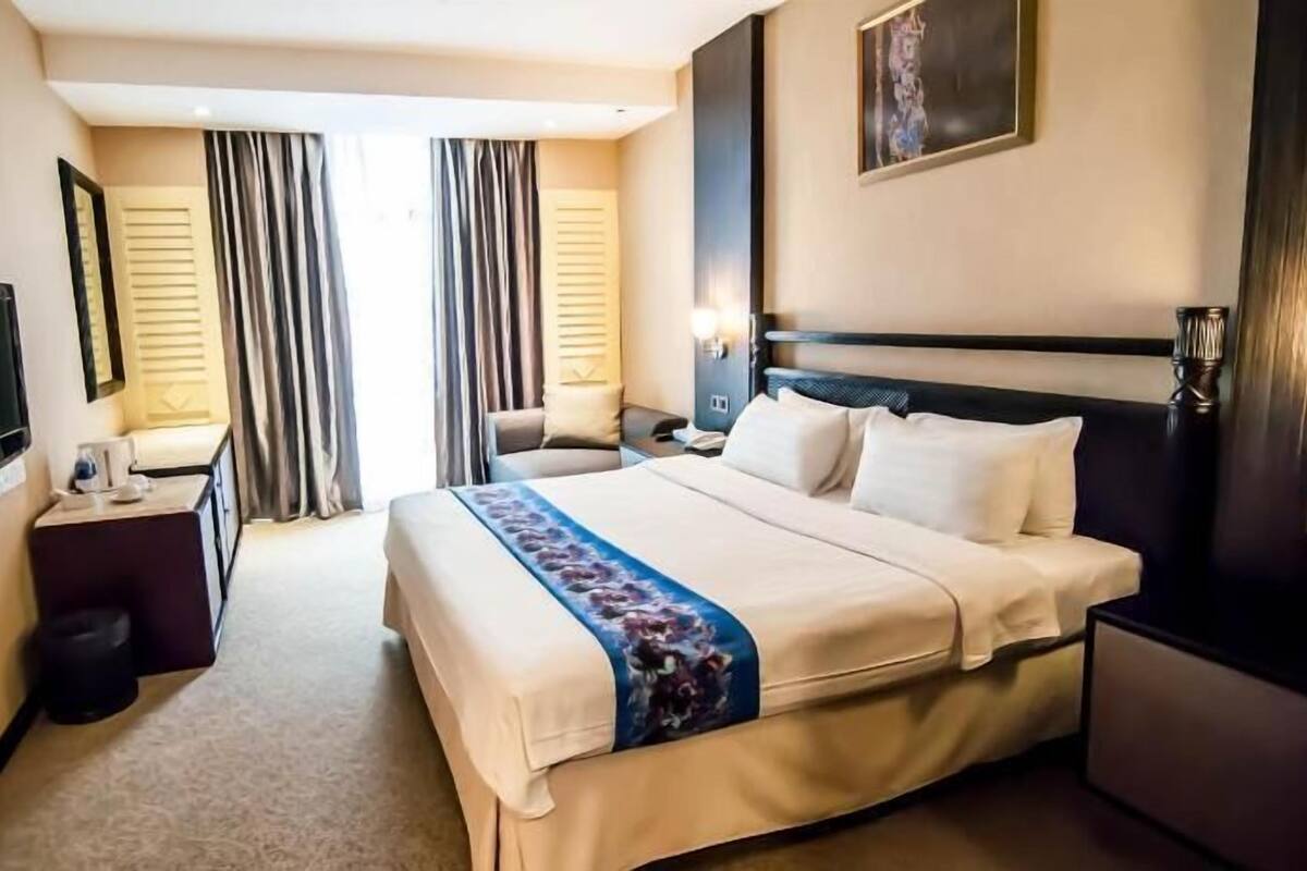 Ein Hotelzimmer mit Bett, Nachttisch, Fernseher, Vorhängen und einem Bild an der Wand.