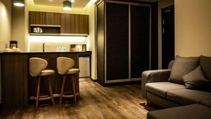 A modern kitchen with wooden cabinets, a bar area with stools, a built-in oven, and a dark sliding door closet. - KK Times Square Hotel (Kota Kinabalu)